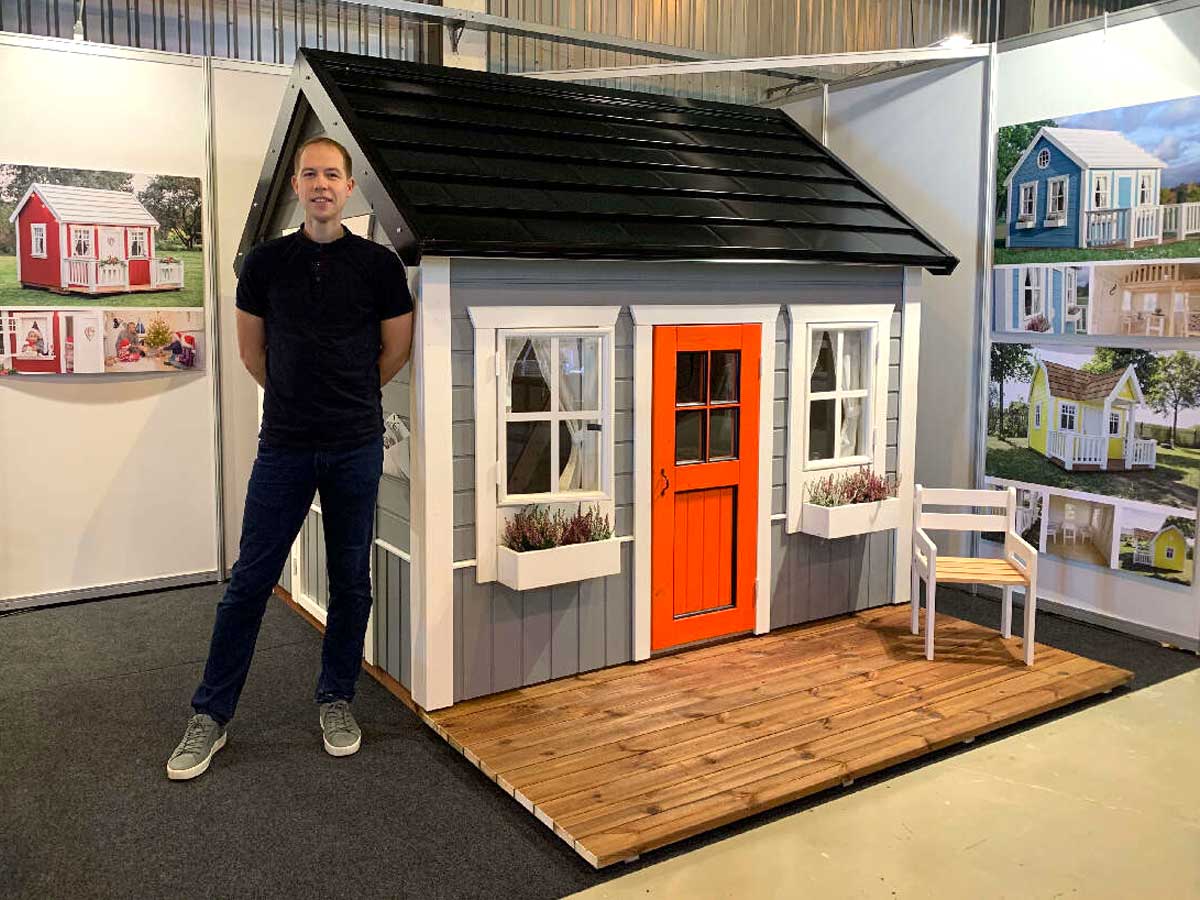 KidsPlayHouses_EU Wooden kids playhouse Boy Cave, with a woodworker standing next to it and a chair on the terrace