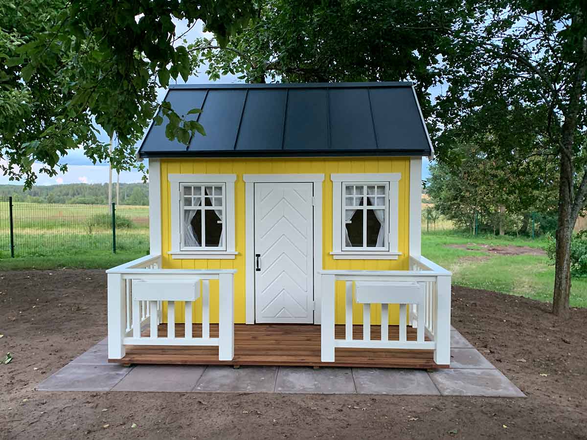KidsPlayHouses_EU yellow playhouse Sunshine front view with white herringbone pattern door, yellow walls, white framed windows, black steel roof and wooden deck with rails