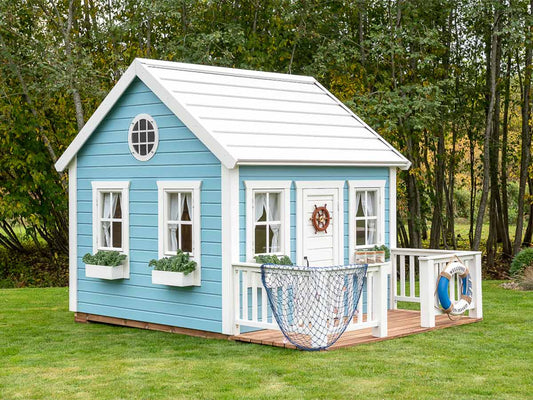 KidsPlayHouses_EU painted playhouse BlueBird with white steel roof, light blue walls, white windows and wooden terrace in backyard