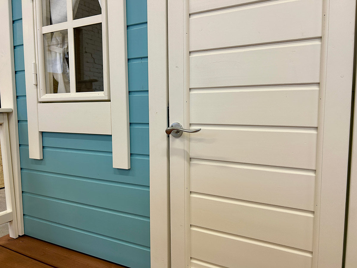 White wooden door and window of a kids’ playhouse with blue pre-painted siding and metal handle