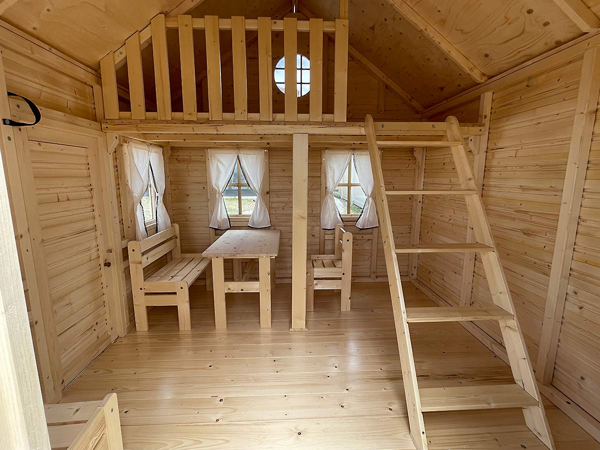 Wooden playhouse with interior details including a staircase, kids play furniture and windows.
