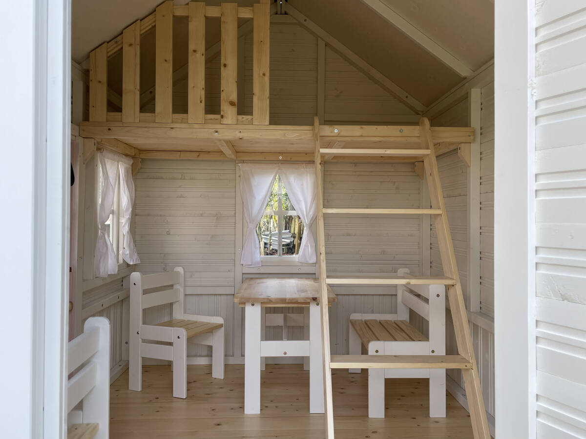 Wooden playhouse with a ladder, table, and chairs inside.