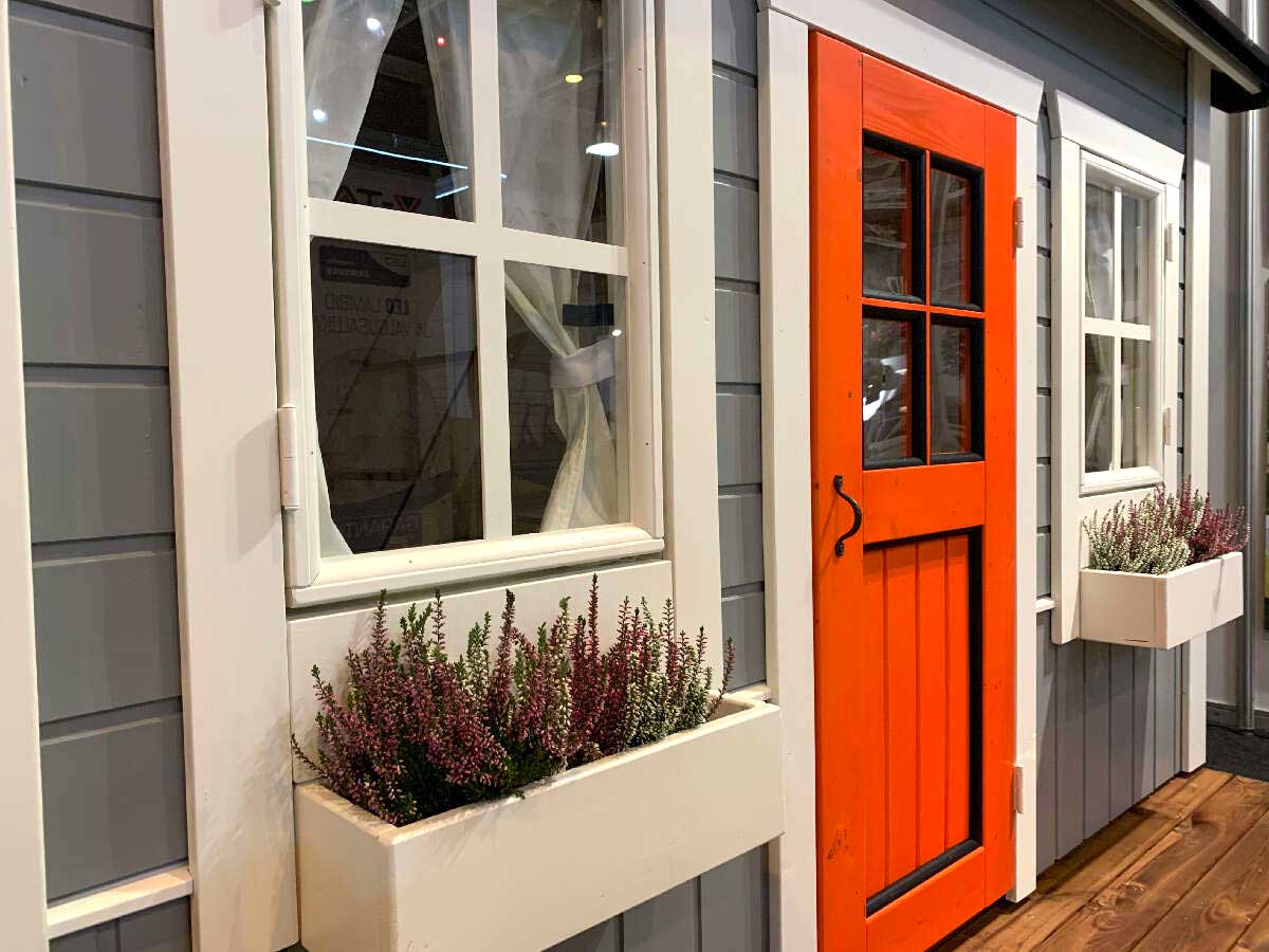 Playhouse with a bright red door and window boxes filled with plants.