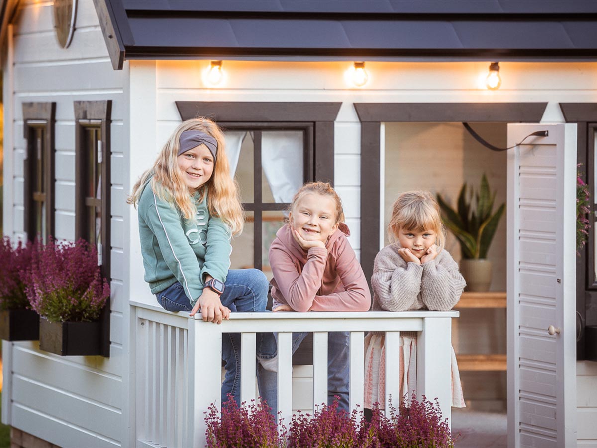 Girls on the wooden terrace with white railing of the KidsPlayhouses_EU quick-assembly playhouse